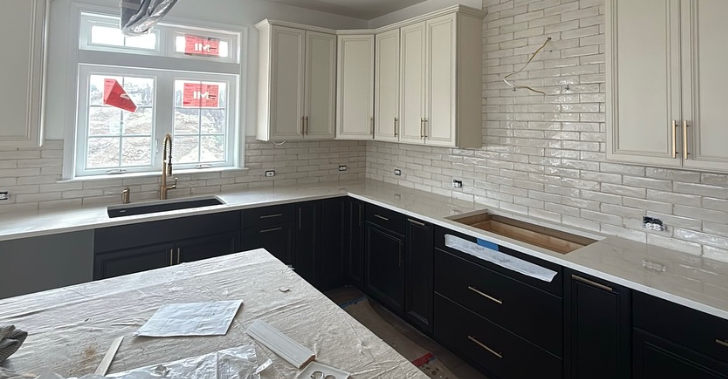 Kitchen under renovation with white cabinets, black lower cabinets, and a light countertop by a window.