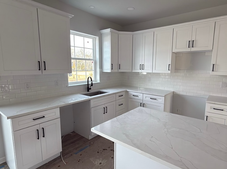 Bright white kitchen with cabinets, island, sink, and large windows in natural light