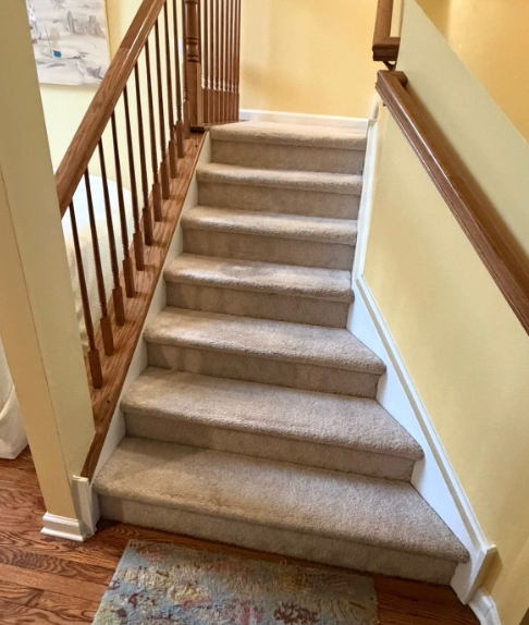 Carpeted indoor staircase with wooden banister and cream-colored walls, viewed from the bottom.