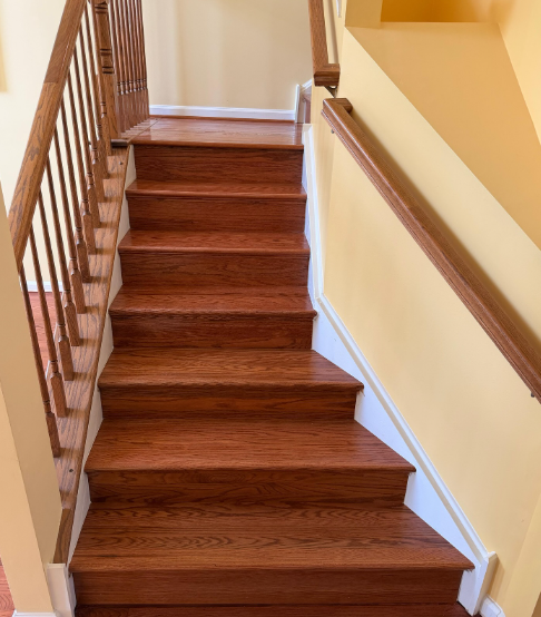 Wooden staircase with brown steps and beige walls, viewed from the bottom landing.