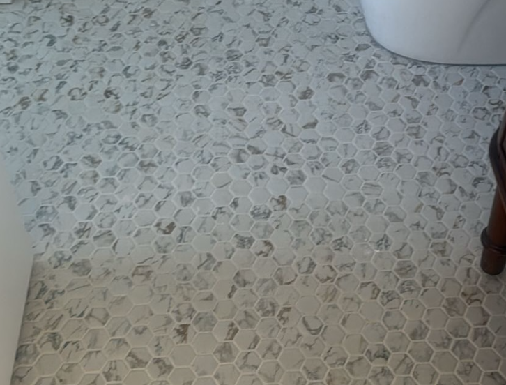 Tiled bathroom floor with a light gray hexagonal pattern, next to a toilet and wooden furniture leg