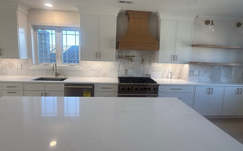 Bright modern kitchen with white countertops, light cabinets, subway tile backsplash, and a large stove hood.