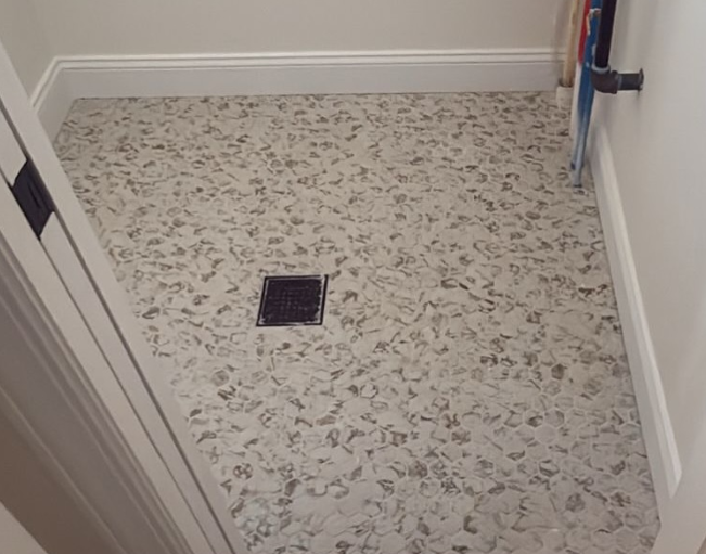 Small utility room with speckled flooring, a floor drain, and a mop or tool leaning against the wall.