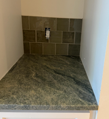 Empty kitchen countertop nook with dark granite, tiled backsplash, and wall outlet above.