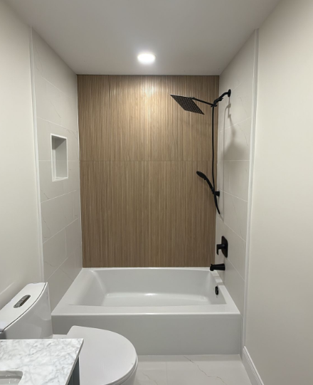 Small modern bathroom with a bathtub, shower, toilet, and wood-paneled wall in a narrow space