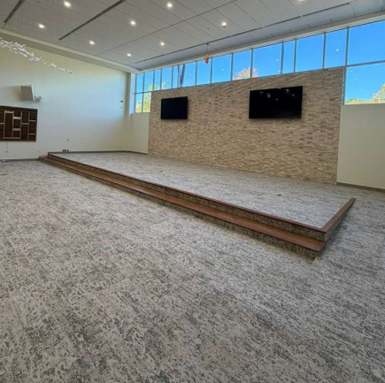 Empty modern room with raised carpeted stage, stone accent wall, and two wall-mounted TVs.