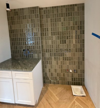 Partially finished kitchen with green tile backsplash, white cabinets, and herringbone wood floor; tile set on floor.