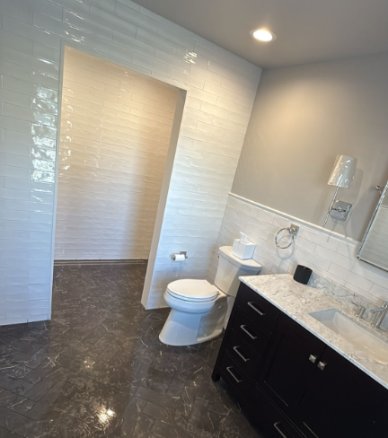 Modern bathroom with dark floor tiles, white walls, black vanity, toilet, and walk-in shower opening