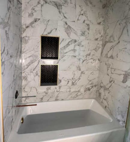 White marble bathroom with a built-in bathtub and two small dark wall niches above it