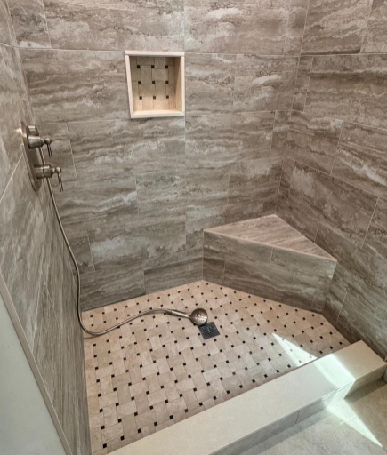 Modern tiled walk-in shower with bench, square niche, and rain showerhead on the wall.