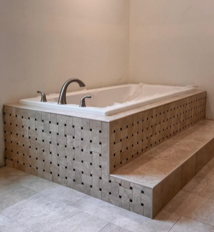 White tiled corner bathtub with chrome fixtures and built-in step in a beige bathroom