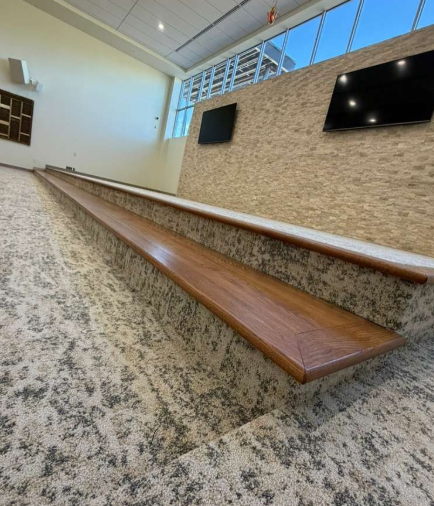 Long wooden bench in a bright hall with stone wall and two wall-mounted TVs