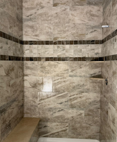 Empty tiled shower with beige stone walls, dark accent bands, and a built-in bench.
