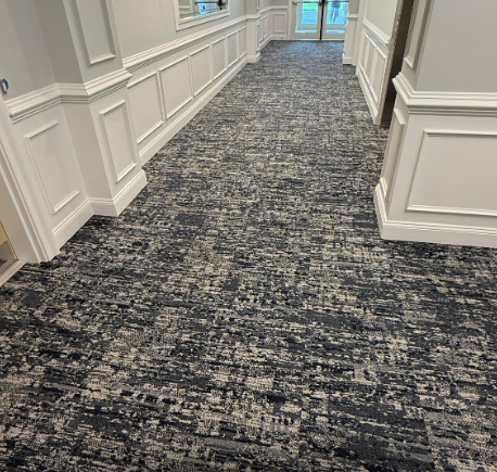 Empty carpeted hallway with white paneled walls and blue-gray patterned flooring