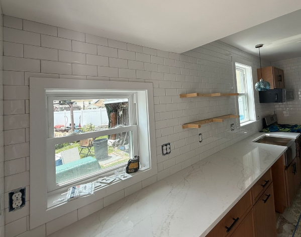 Bright kitchen with white subway tile, open shelves, window, and a long countertop under installation