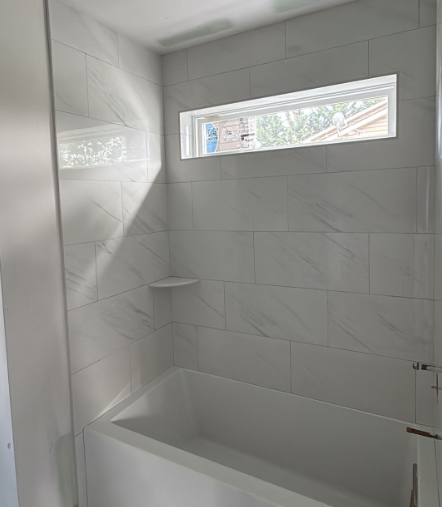 White tiled bathroom with a bathtub and a narrow frosted window above it.