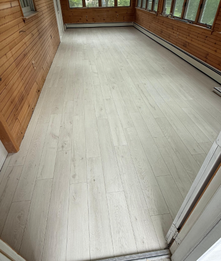 Empty sunroom with light wood walls, large windows, and pale wood flooring.