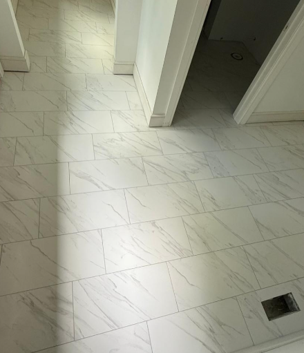 White tiled hallway with open doorways and a floor drain near the bottom right.