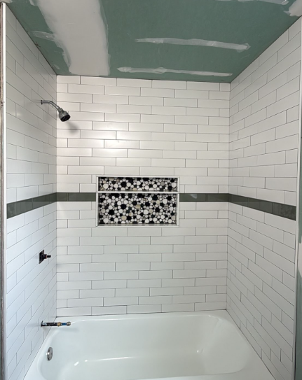 White-tiled shower and bathtub with gray accent band and green unfinished ceiling patch
