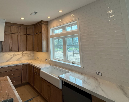 Modern kitchen with wood cabinets, marble countertops, white tile backsplash, and a farmhouse sink under a window