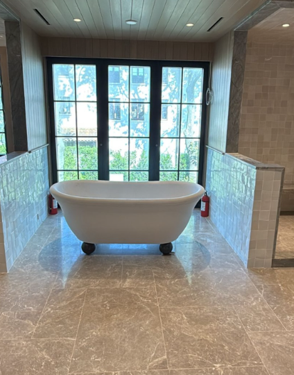 Modern bathroom with freestanding white tub before large windows and glass shower on marble floor