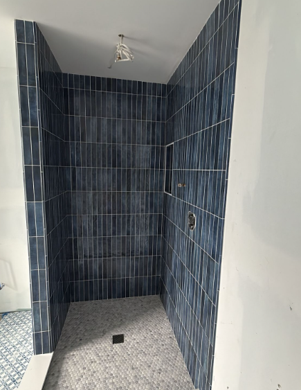 Narrow tiled shower stall with dark blue walls, gray floor, and a single ceiling light.