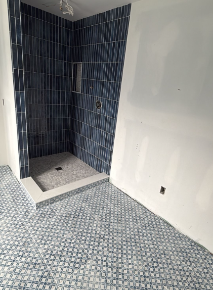 Small tiled bathroom under renovation with blue shower stall and mosaic floor.