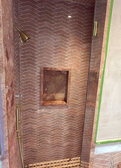 Brown tiled shower wall with a recessed niche and a green-trimmed doorway edge