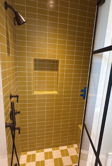 Yellow-tiled shower with a built-in niche, black fixtures, and a glass door.