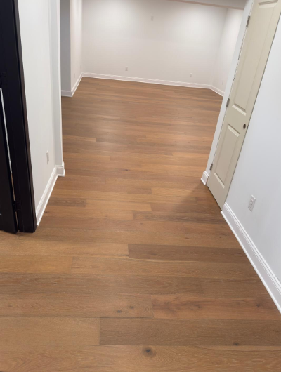 Empty hallway with brown wood floors, white walls, and open doors.