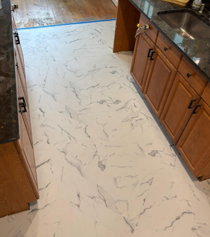 White marble-look floor installed in a kitchen with wooden cabinets and a stainless sink.