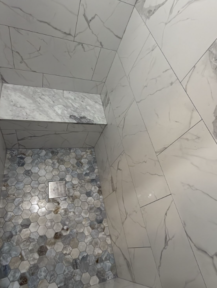 Marble-tiled shower with hexagon pebble floor and wall niche shelf