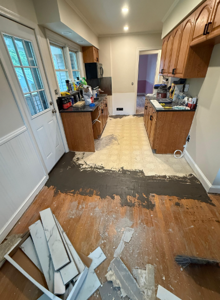 Renovating kitchen with damaged wood floor, cabinets along both sides, and debris in foreground