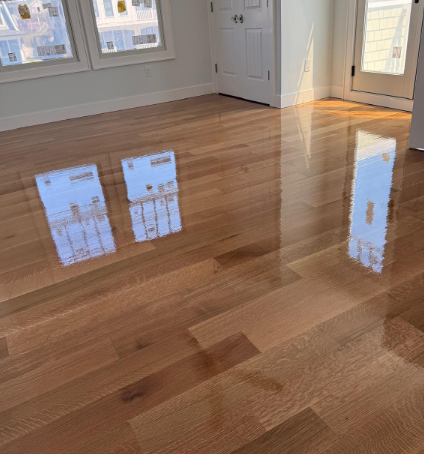 Sunlit empty room with glossy hardwood floors and white walls, reflecting the windows and door.