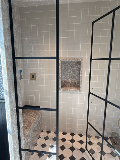 Small tiled bathroom with black metal stall frames and a black-and-white hexagonal floor.