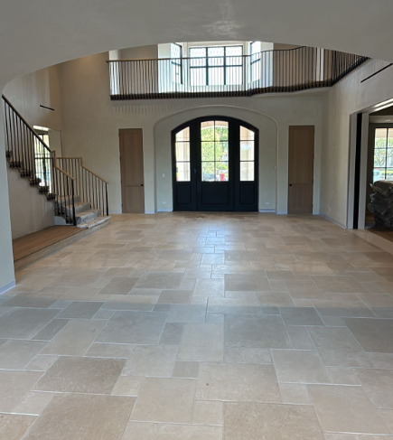 Spacious foyer with tiled floor, curved staircase, and large double doors under an upper balcony.