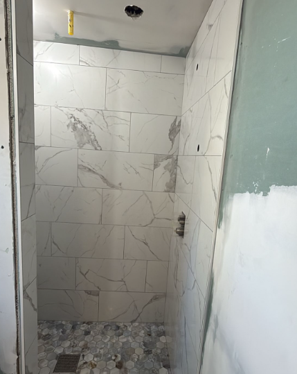 Partially tiled shower stall with unfinished walls and debris on the floor