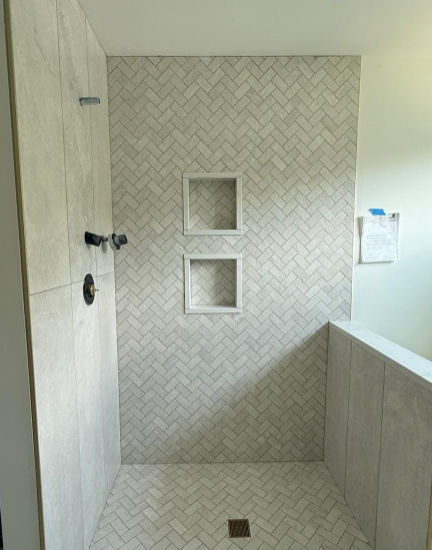 Bathroom shower stall with herringbone tile, two recessed niches, and a floor drain