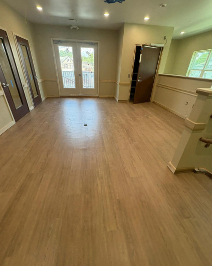 Empty room with light wood flooring, beige walls, windows, and an open door to a bathroom.