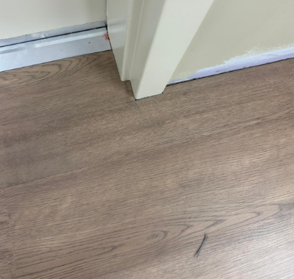 Floor and white doorframe at a threshold, with wood-look flooring and baseboard trim.