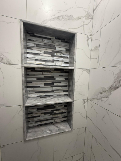 Built-in tiled shower niche with three shelves and gray mosaic accent tile run