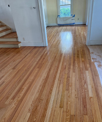 Empty hallway with freshly refinished hardwood floors and a window at the far end