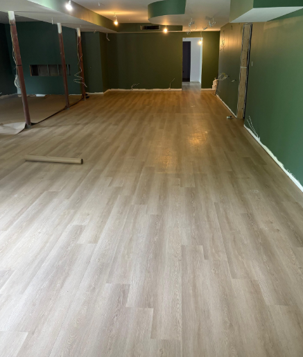 Empty room with light wood flooring, dark green walls, and ceiling lights during renovation