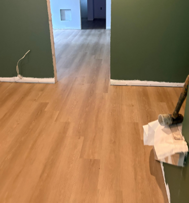 Freshly installed wood floor in a room with green walls and a vacuum leaning on the right side.