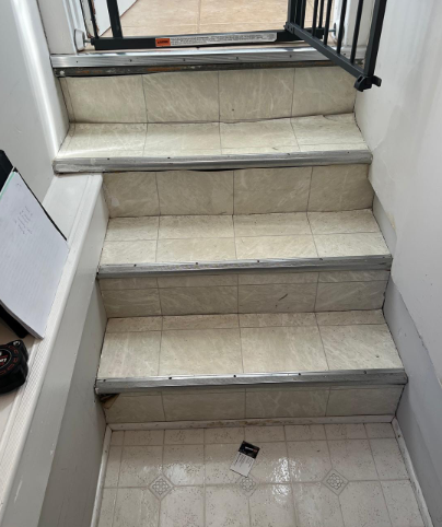 Indoor tiled staircase with four steps and a black metal safety gate at the top