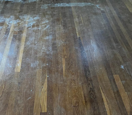 Worn hardwood floor with scattered white dust or residue across several planks