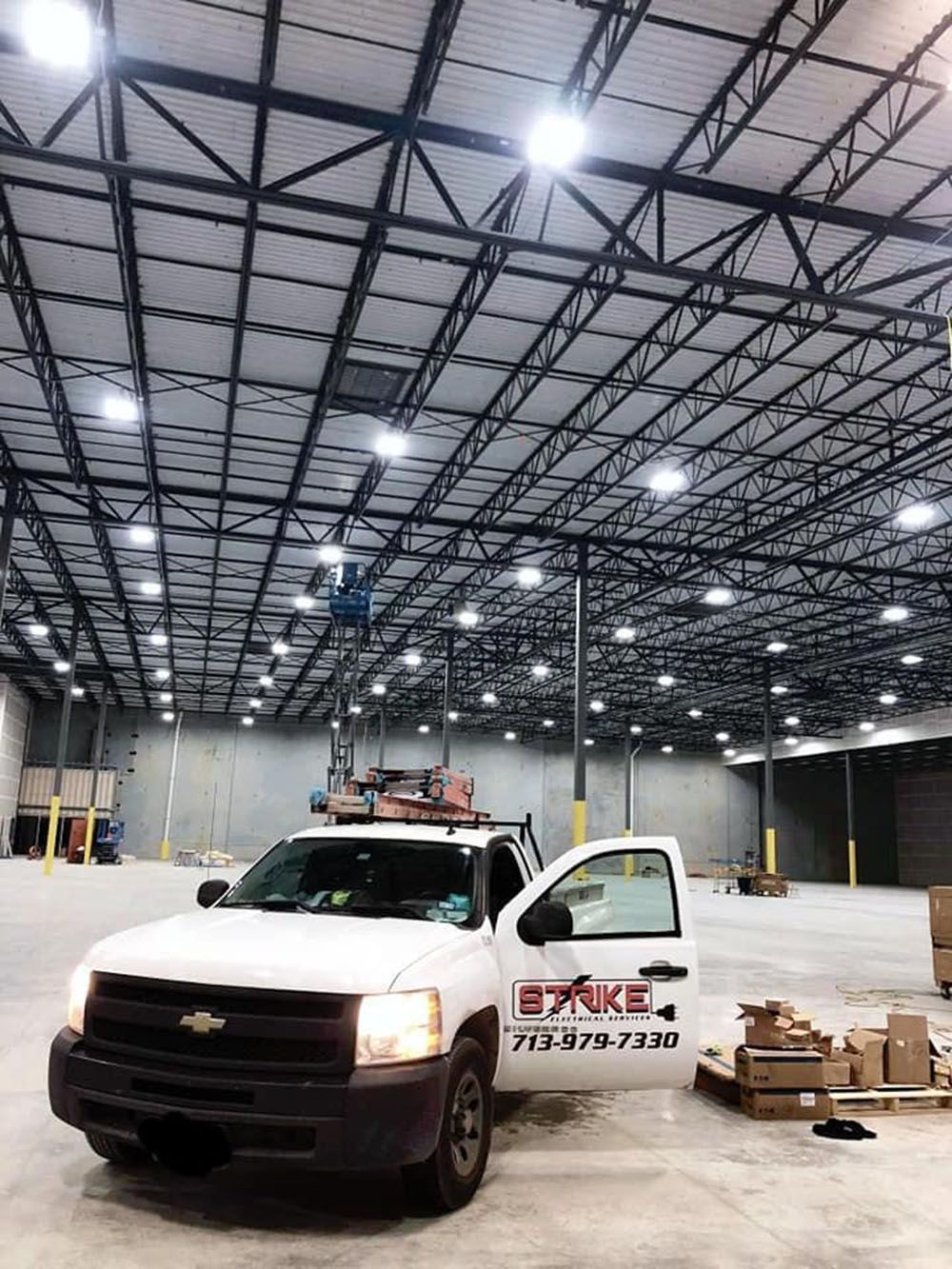 A white truck is parked in a large warehouse with lots of lights installed