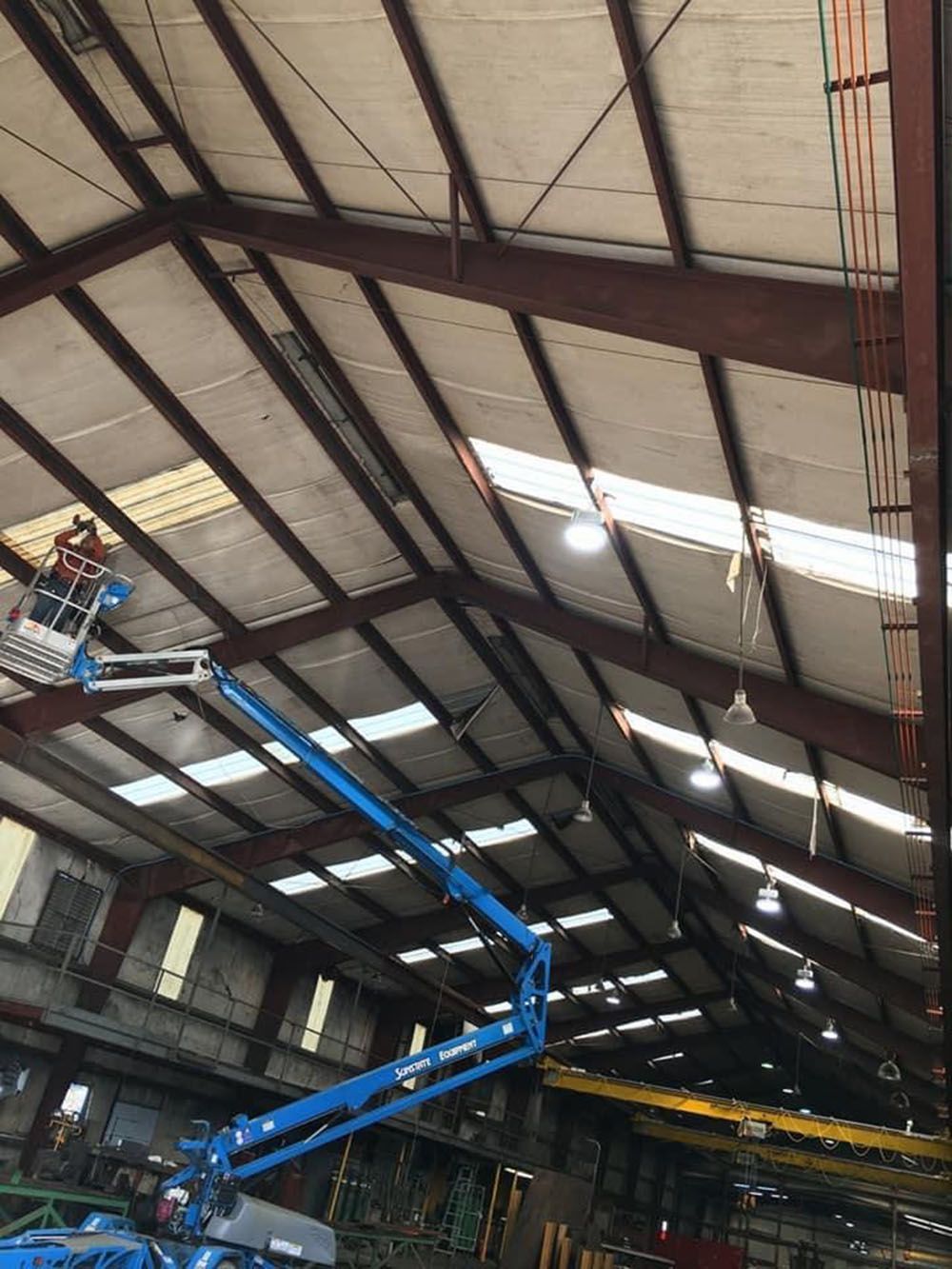 A man on a blue crane is working on the ceiling of a building
