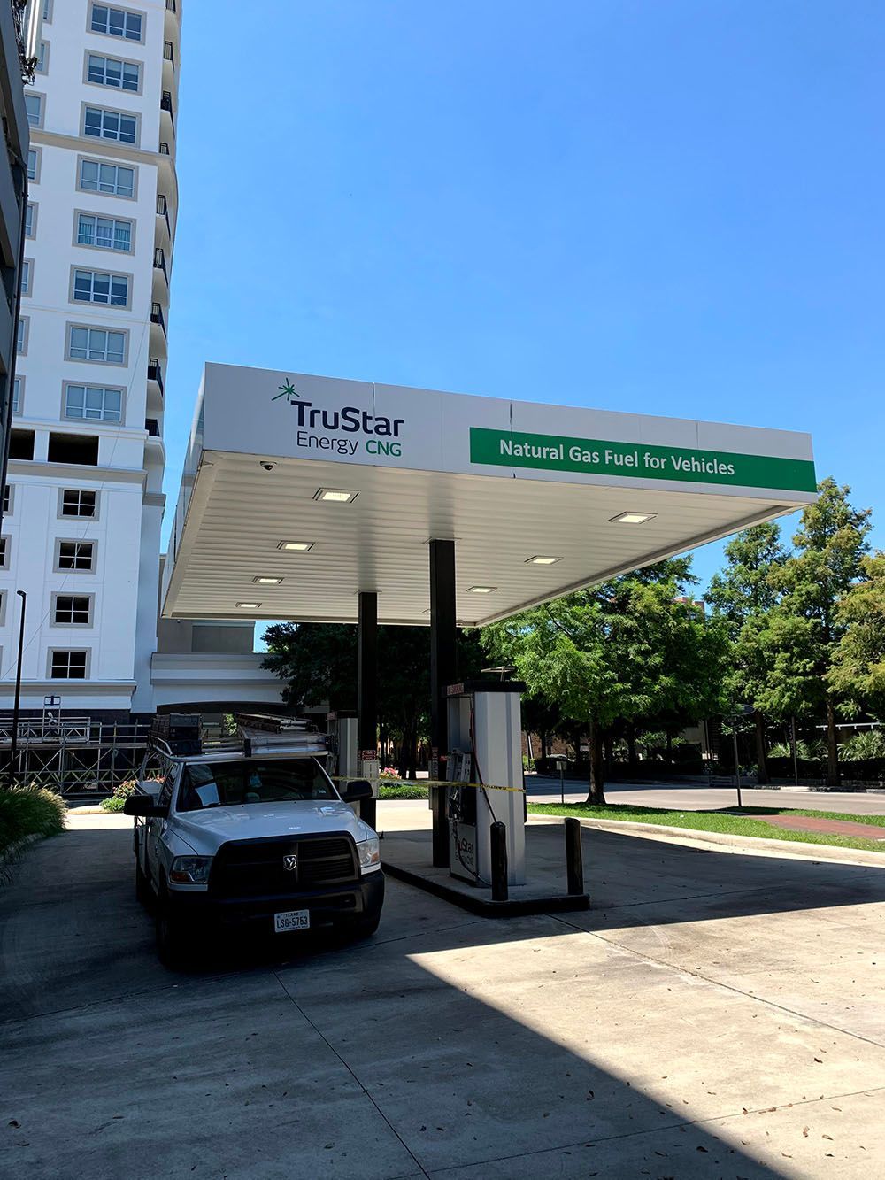 A white truck is parked under a canopy at a gas station
