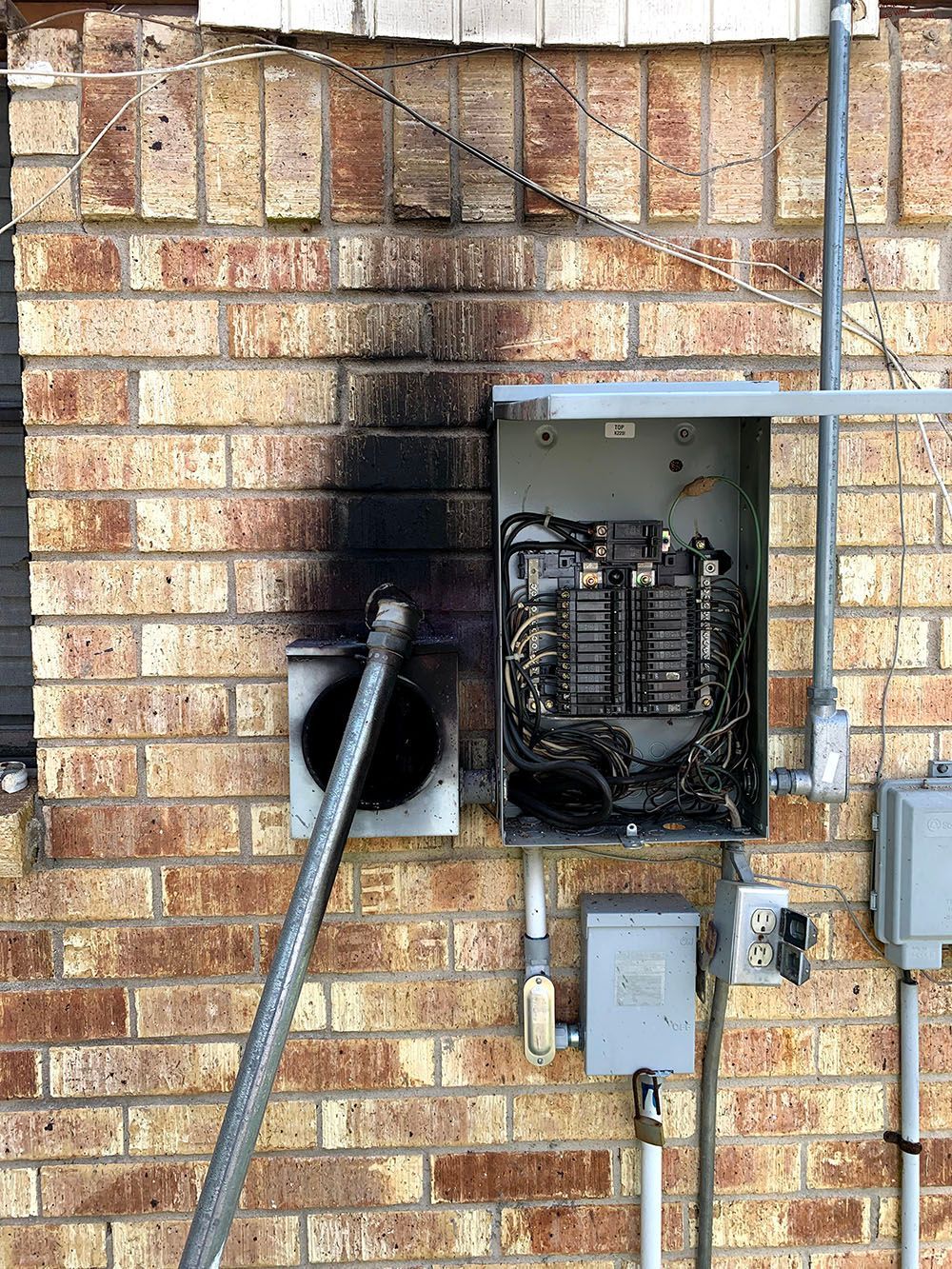 A brick wall with a broken electrical box on it